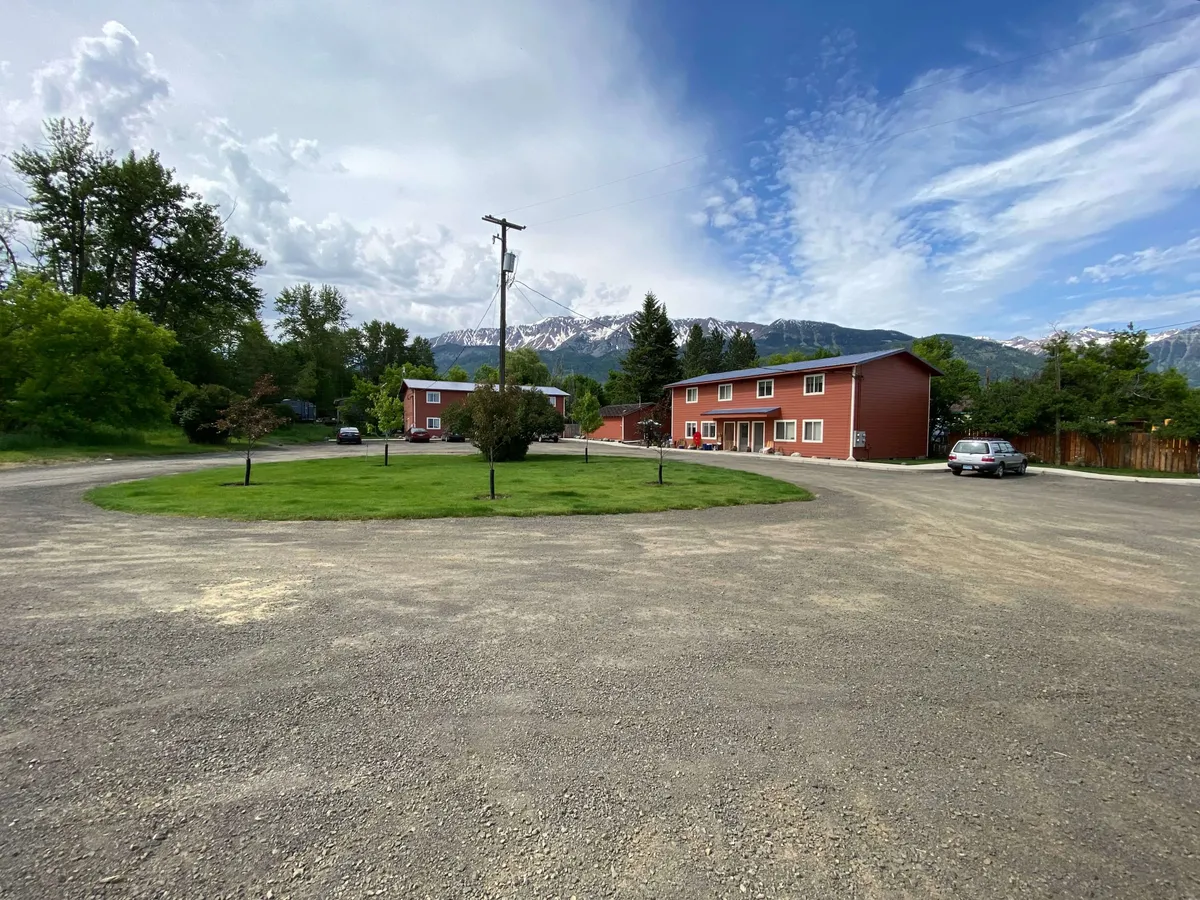Featuring classic red buildings with a dramatic mountain backdrop, lush green grass, and an inviting driveway, this image conveys a sense of open space and natural beauty. The scene hints at the broader surroundings of Joseph, including outdoor gathering areas and nearby attractions.