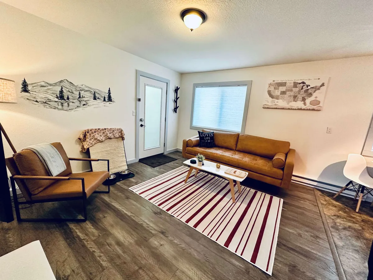 A brown leather couch sits atop a striped rug, facing a striking mountain mural. The space is perfect for curling up with a book, watching TV, or sharing stories with loved ones. The mural and decor create a relaxed, cozy vibe, with plenty of natural light enhancing the area.