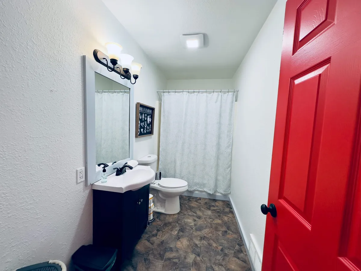 This bathroom scene features a bold red door, a tidy sink area, a mirror, a toilet, and a shower curtain. The space feels fresh and inviting, ideal for personal routines and relaxation after a long day.