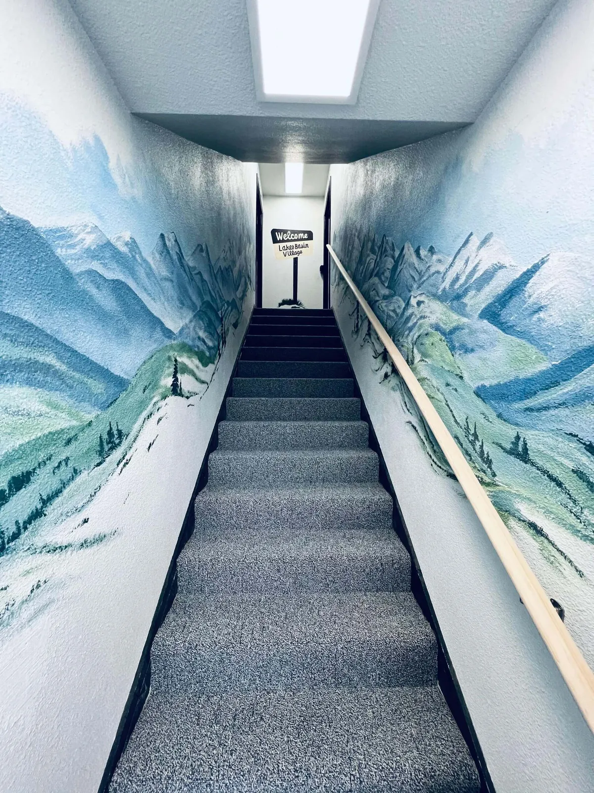 This image features the welcoming entrance area of the property, with a brightly colored mural along the walls, a prominent staircase, and a visible 'welcome' sign. Guests are seen exploring the space, engaging with the artwork, and socializing, which creates an inviting and lively atmosphere. The mural and layout give a strong first impression of the property's connection to its surroundings.